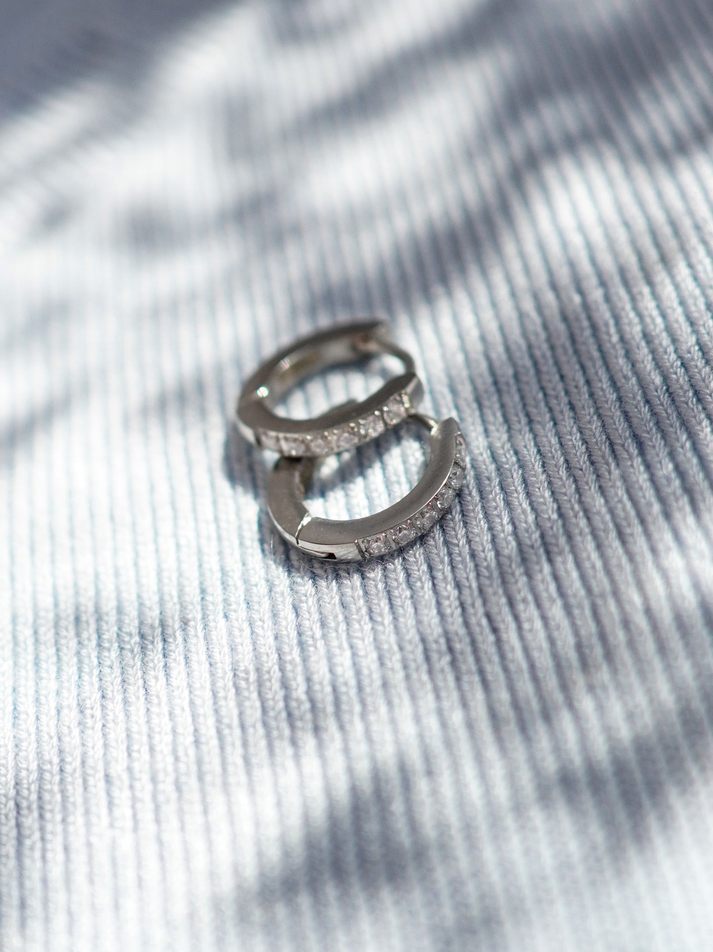 Silver earrings with small crystals on a textured gray surface
