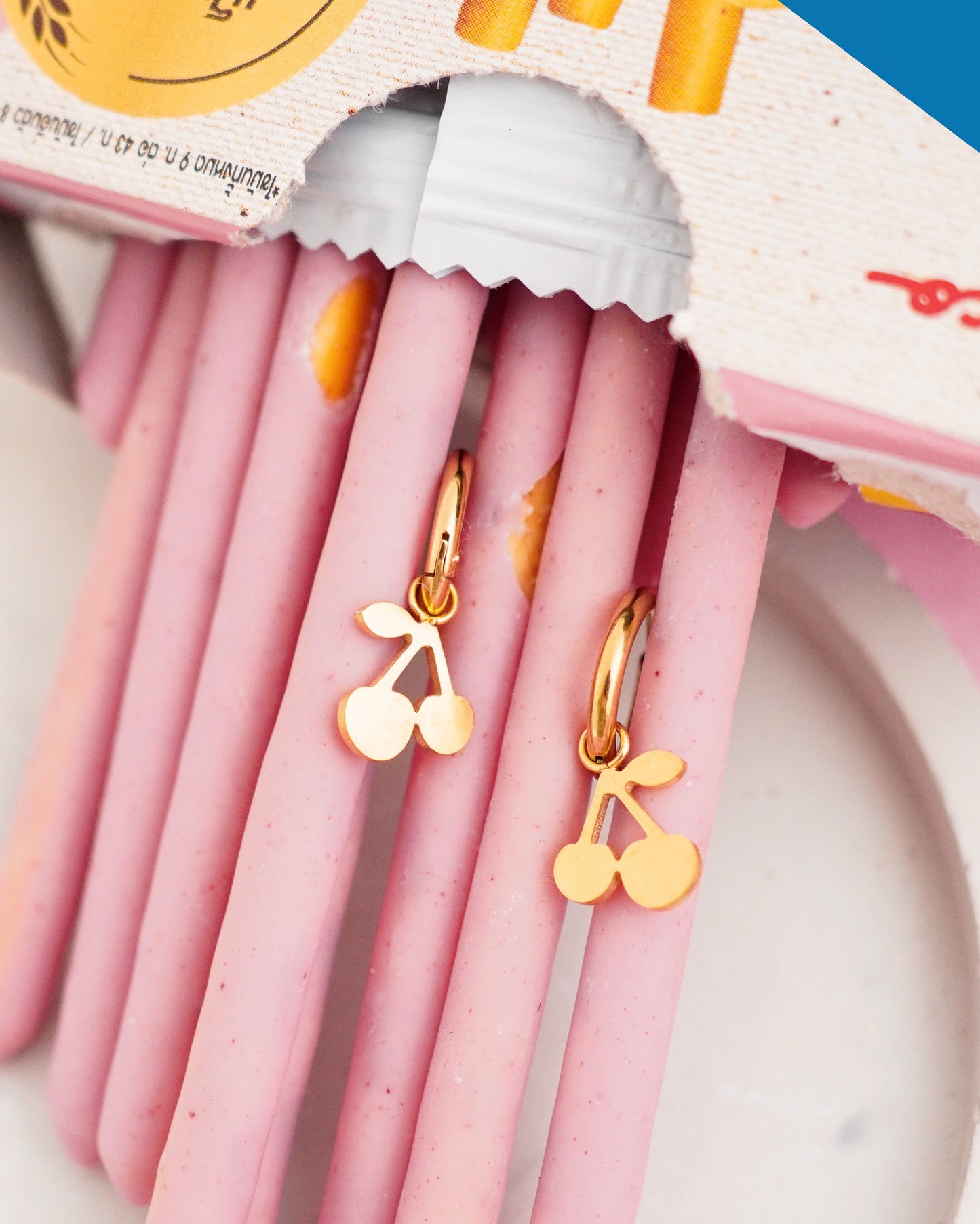 Pink gel pens with gold cherry-shaped earrings on a white background