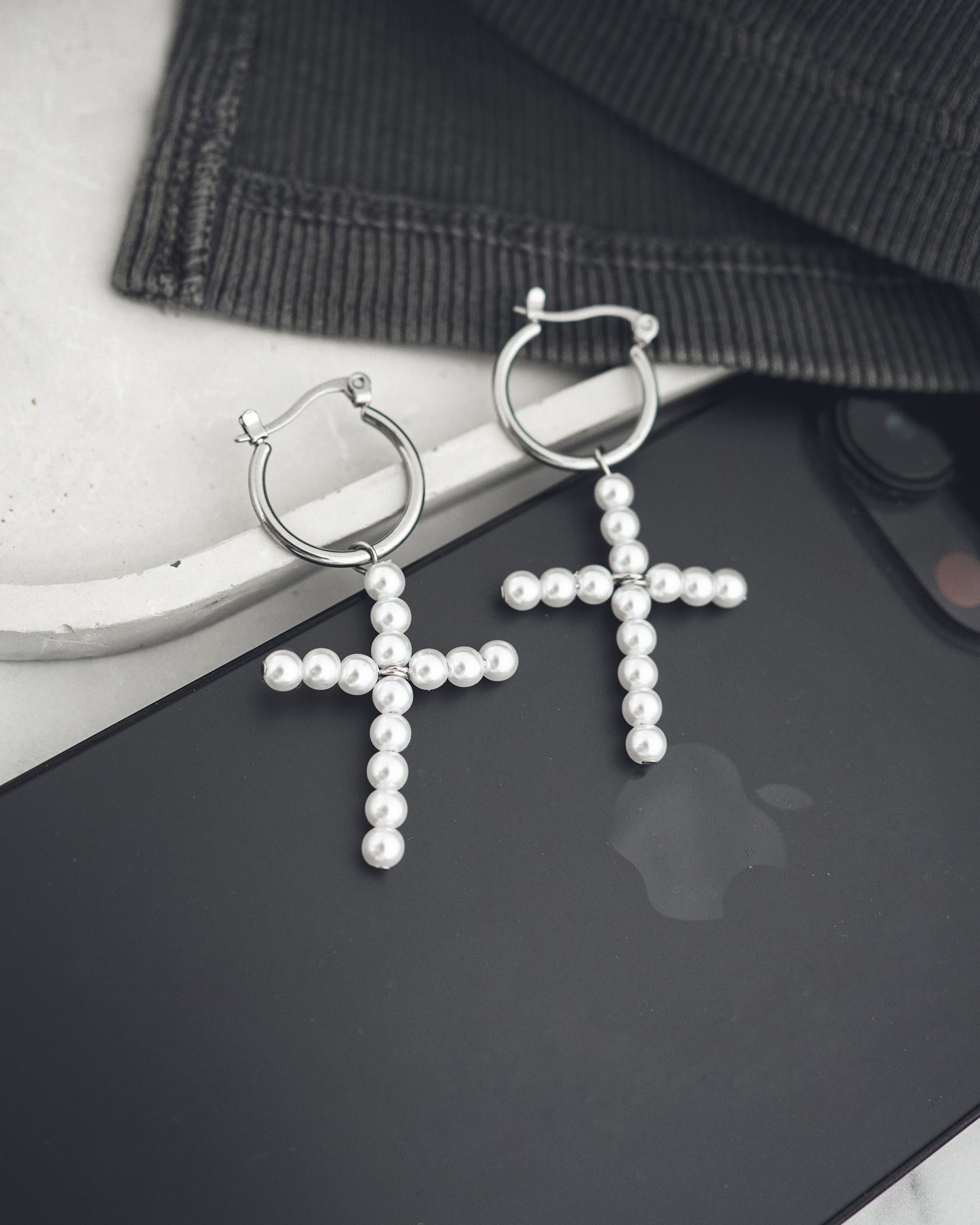 Pearl cross earrings on a black surface with a blurred background