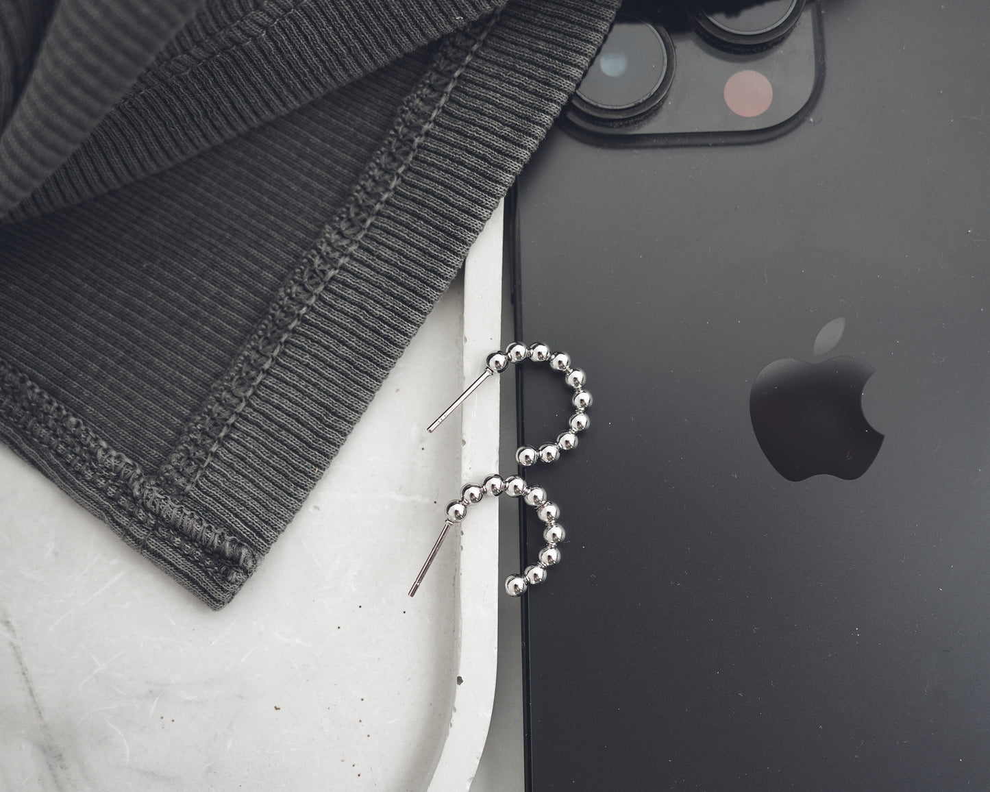 Black smartphone with Apple logo next to a black beaded earring on a white surface