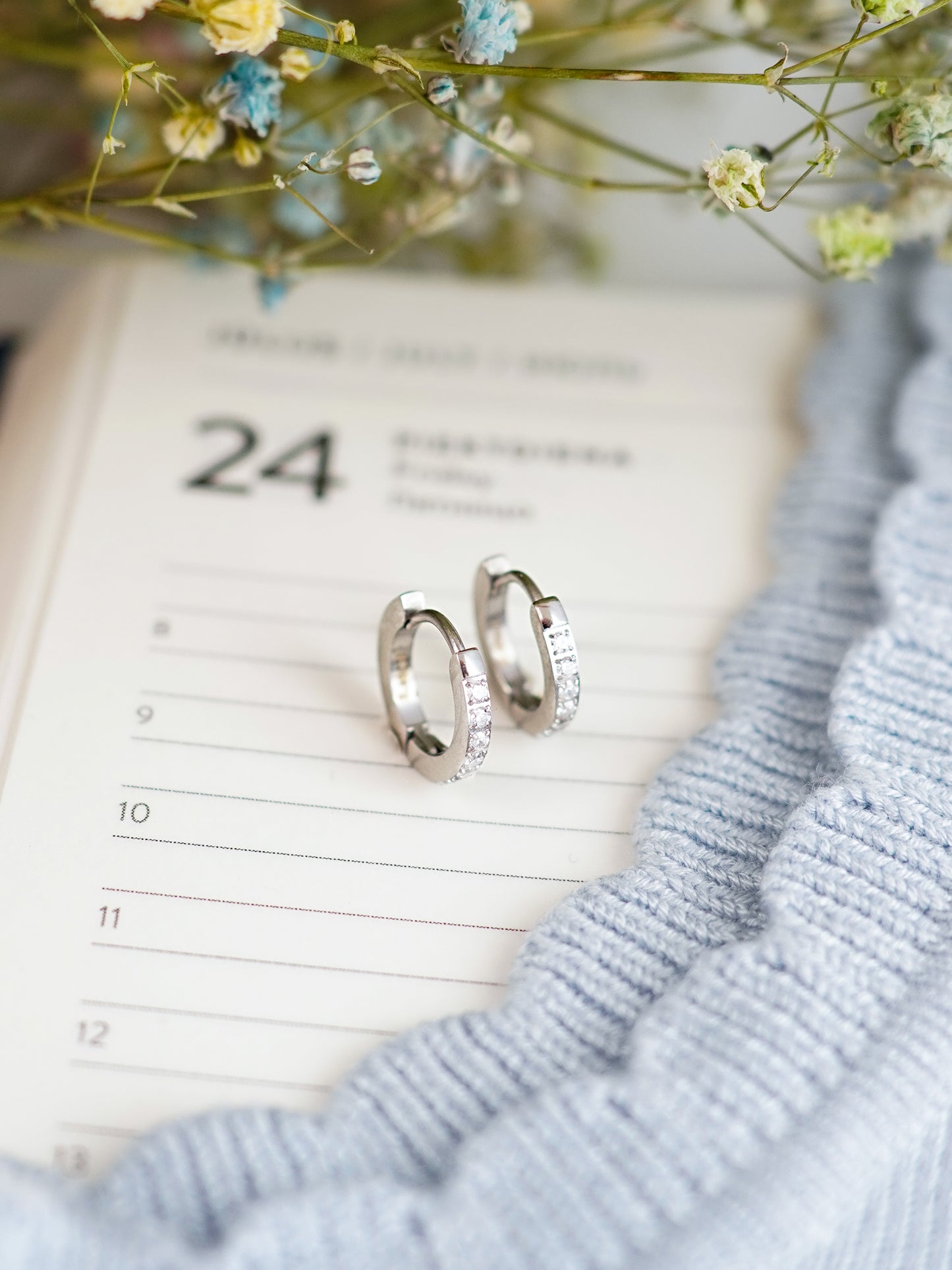 Silver hoop earrings on a calendar with flowers and a blue fabric background