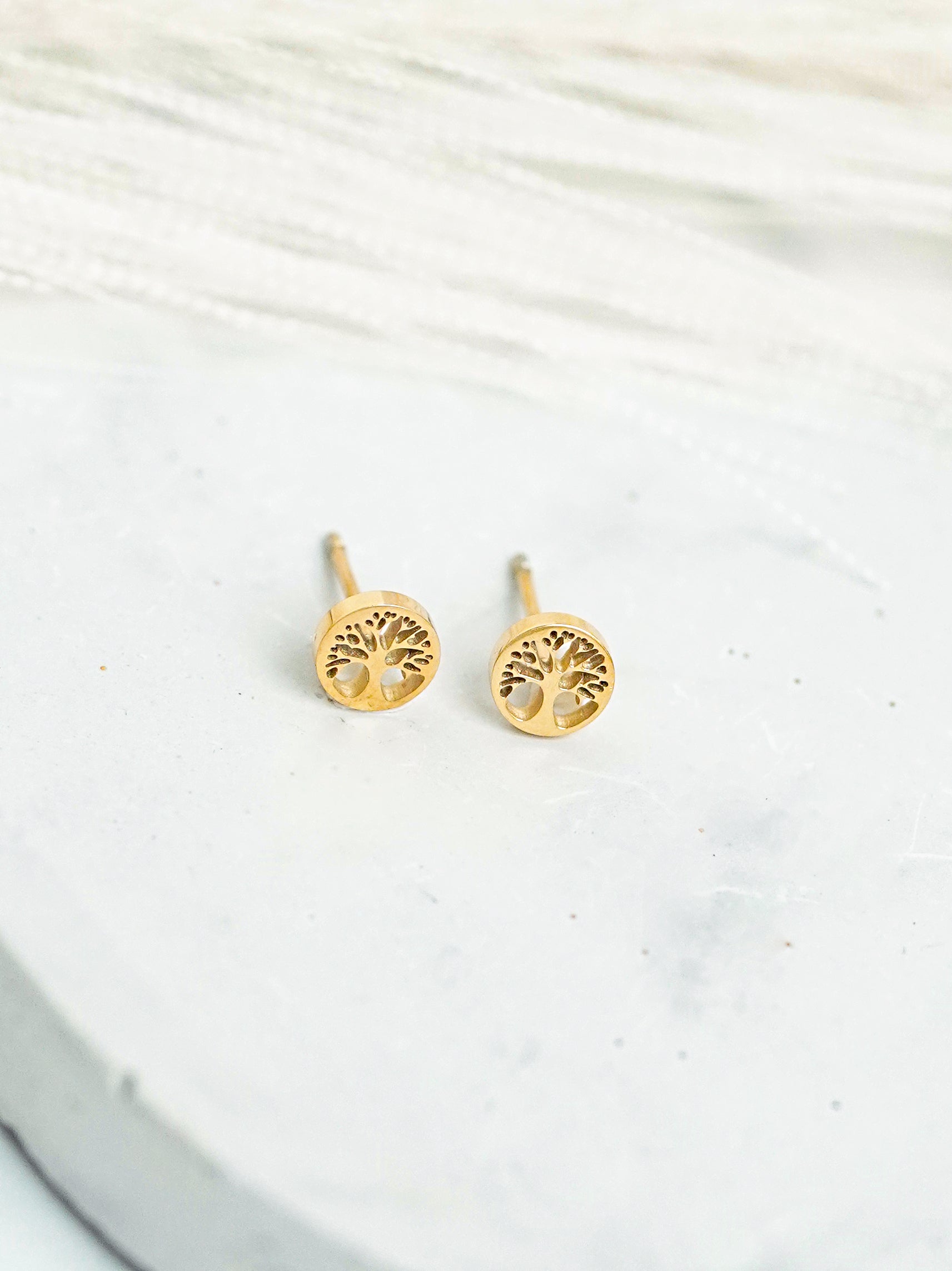 Gold-plated tree-shaped earrings on a white fabric background