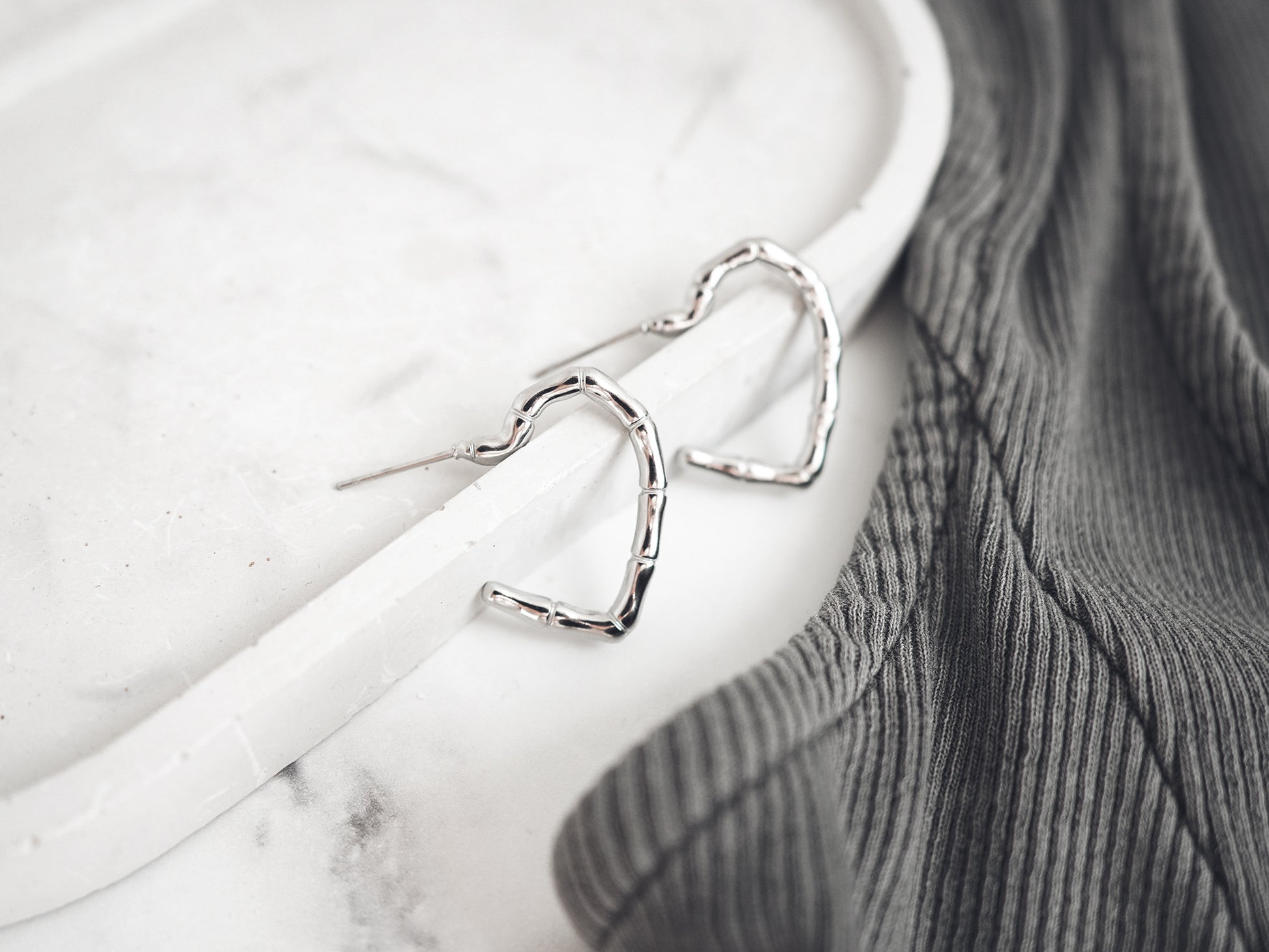Silver heart-shaped earrings on a white marble surface with a gray fabric background