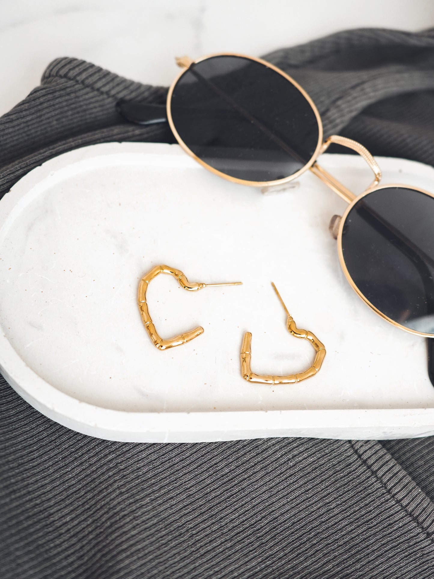 Gold colored heart-shaped earrings on a white surface with sunglasses in the background