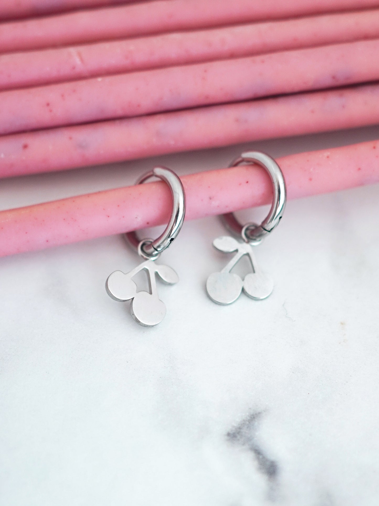 Silver plated hoop earrings with cherry charms on pink straws against a marble background