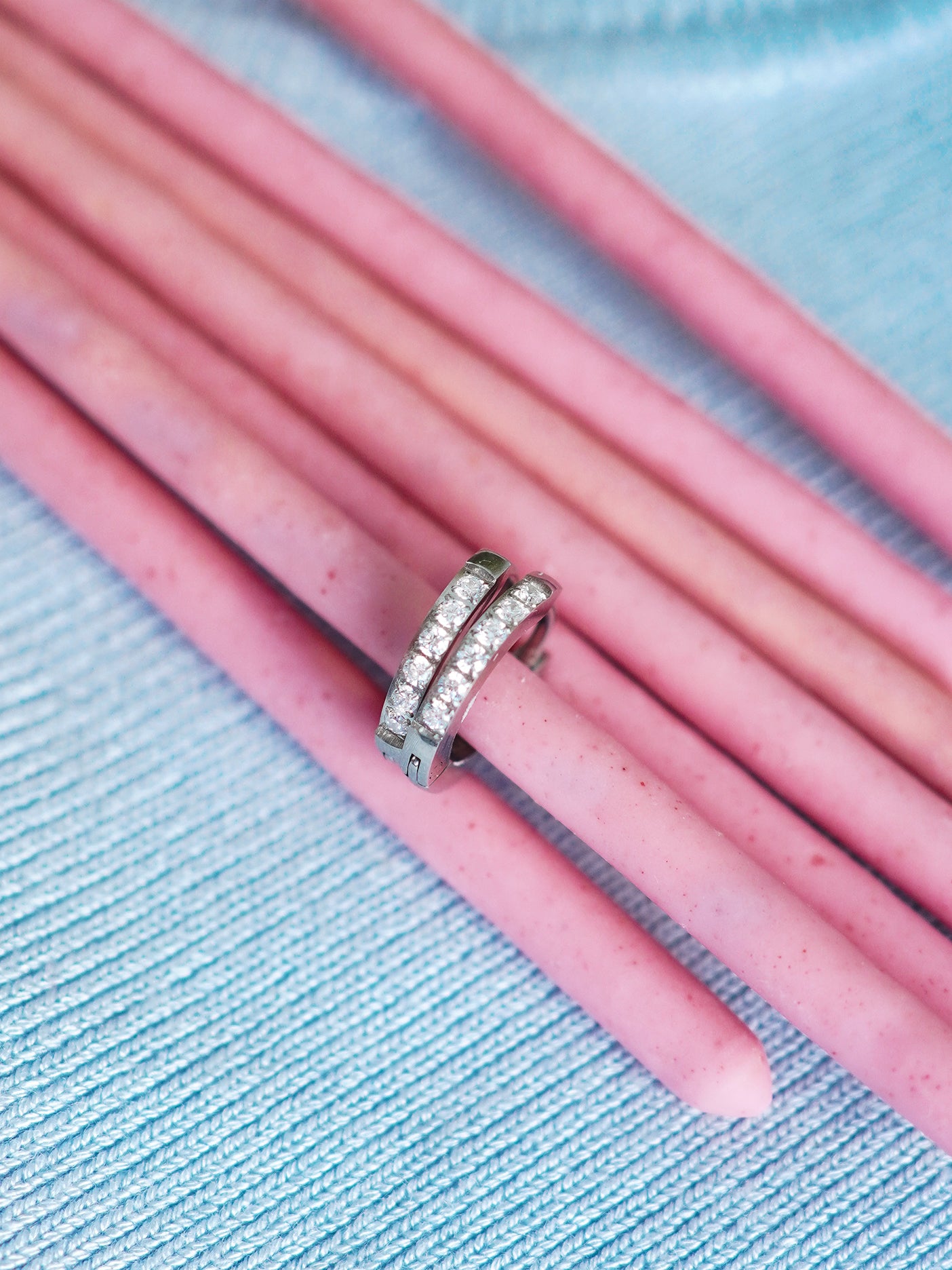 Silver earrings on pink pencils against a blue textured background