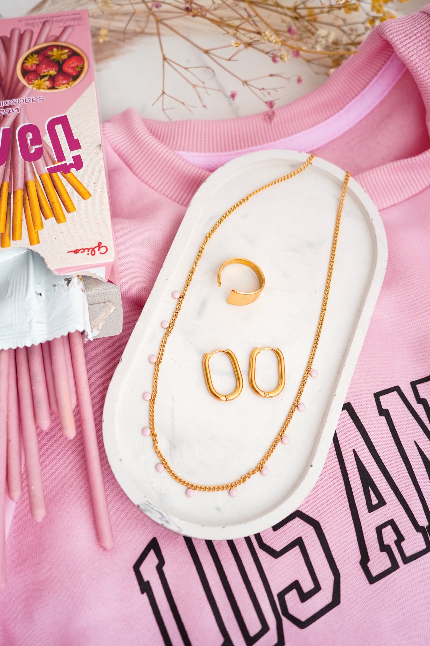 Gold-plated ring, necklace and earrings on a pink sweatshirt with visible text