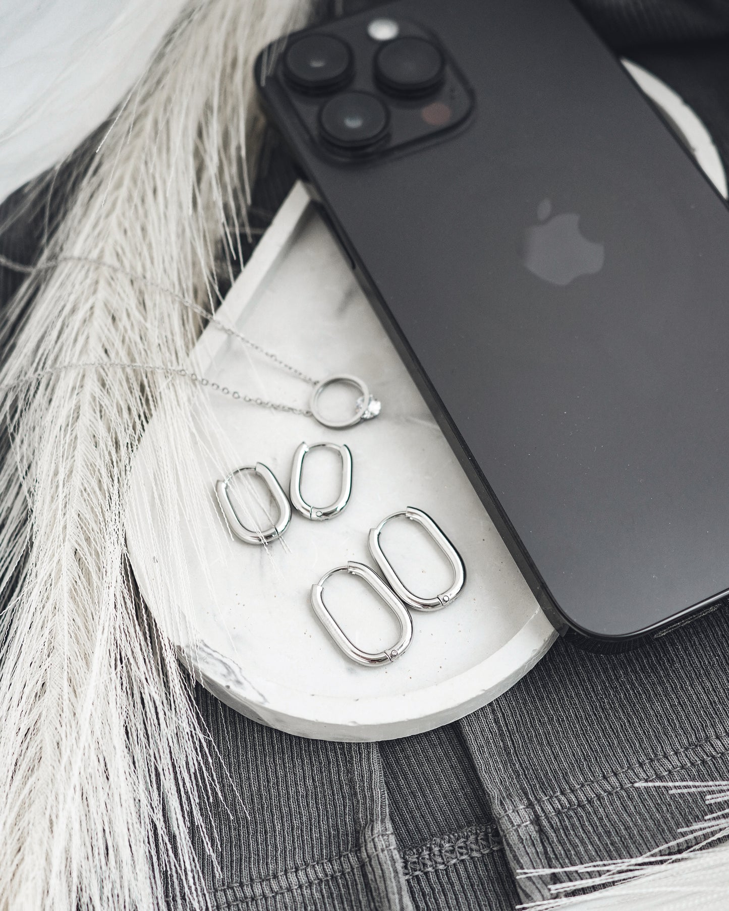 Silver earrings on a white surface with a black phone and gray fabric background