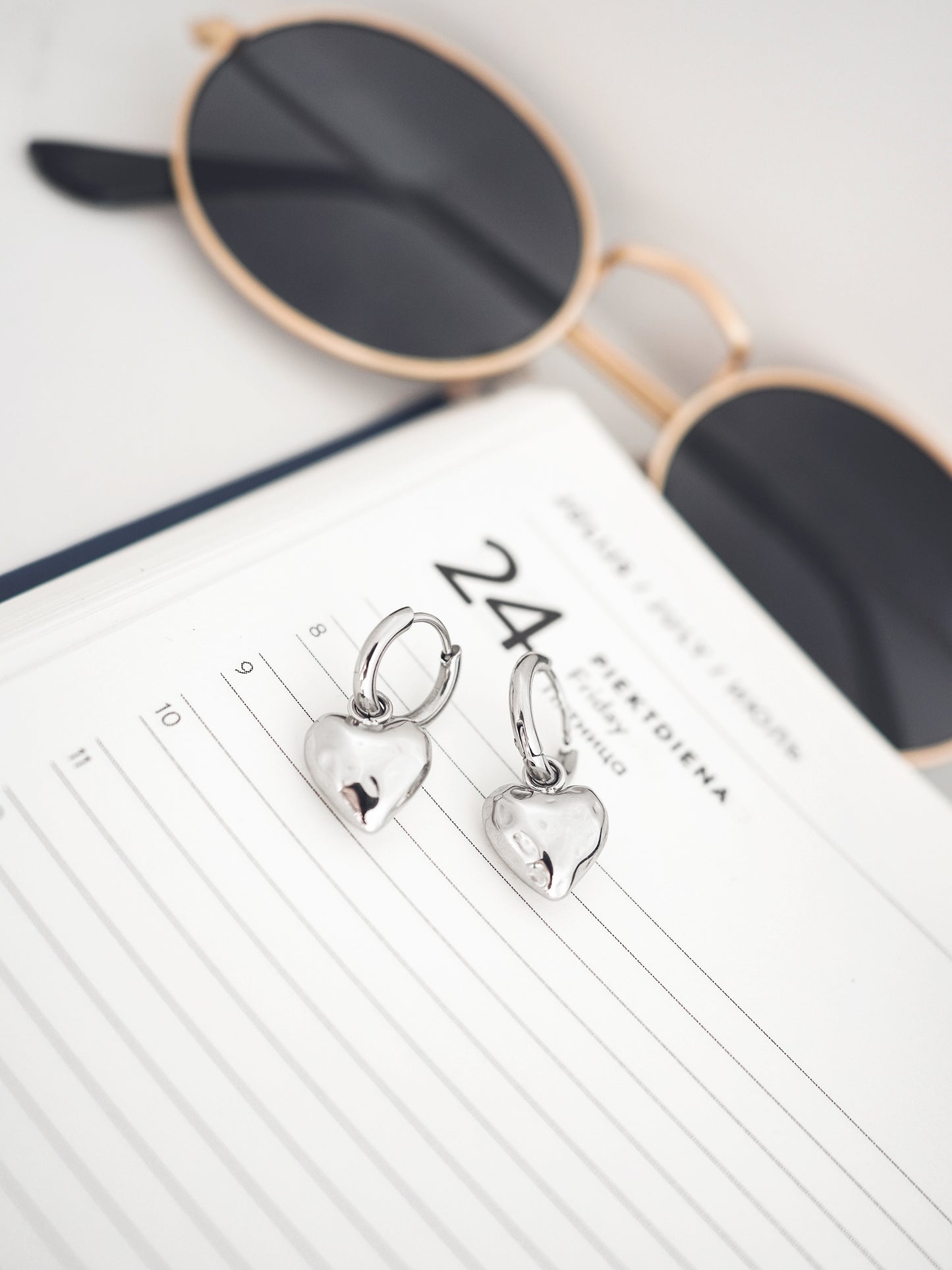 Heart-shaped earrings on a notebook with sunglasses in the background