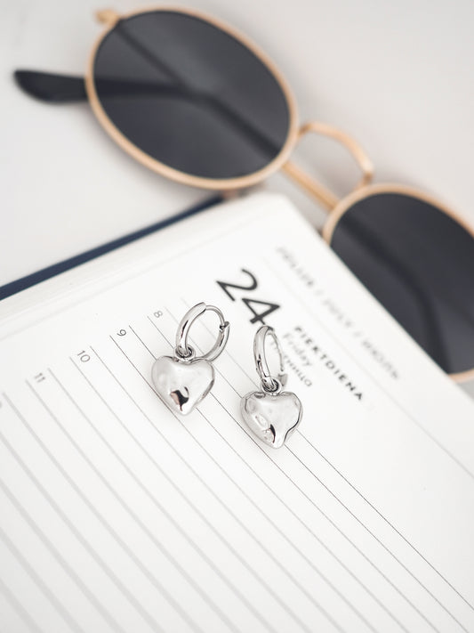 Heart-shaped earrings on a notebook with sunglasses in the background