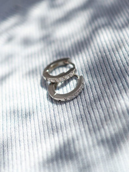 Silver earrings with small crystals on a textured gray surface