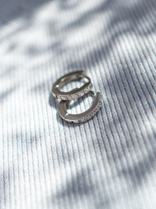 Silver earrings with small crystals on a textured gray surface