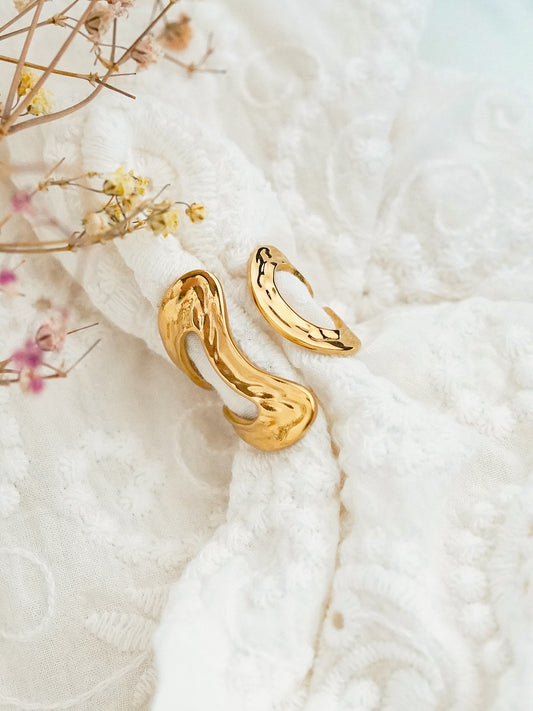 Gold-plated bold ring on a textured white surface with dried flowers.