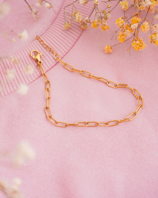 Gold chain bracelet on a pink fabric background with yellow flowers