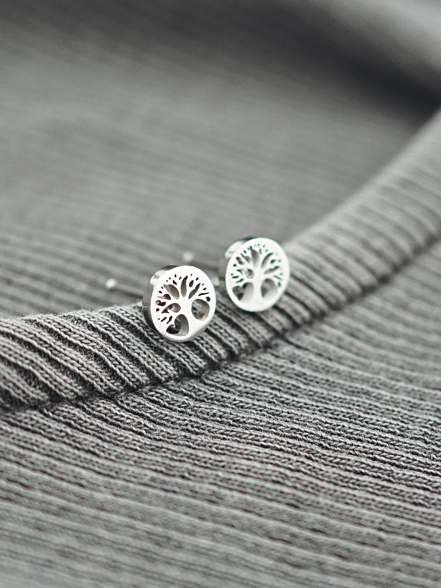 Silver tree-shaped earrings on a gray textured fabric background