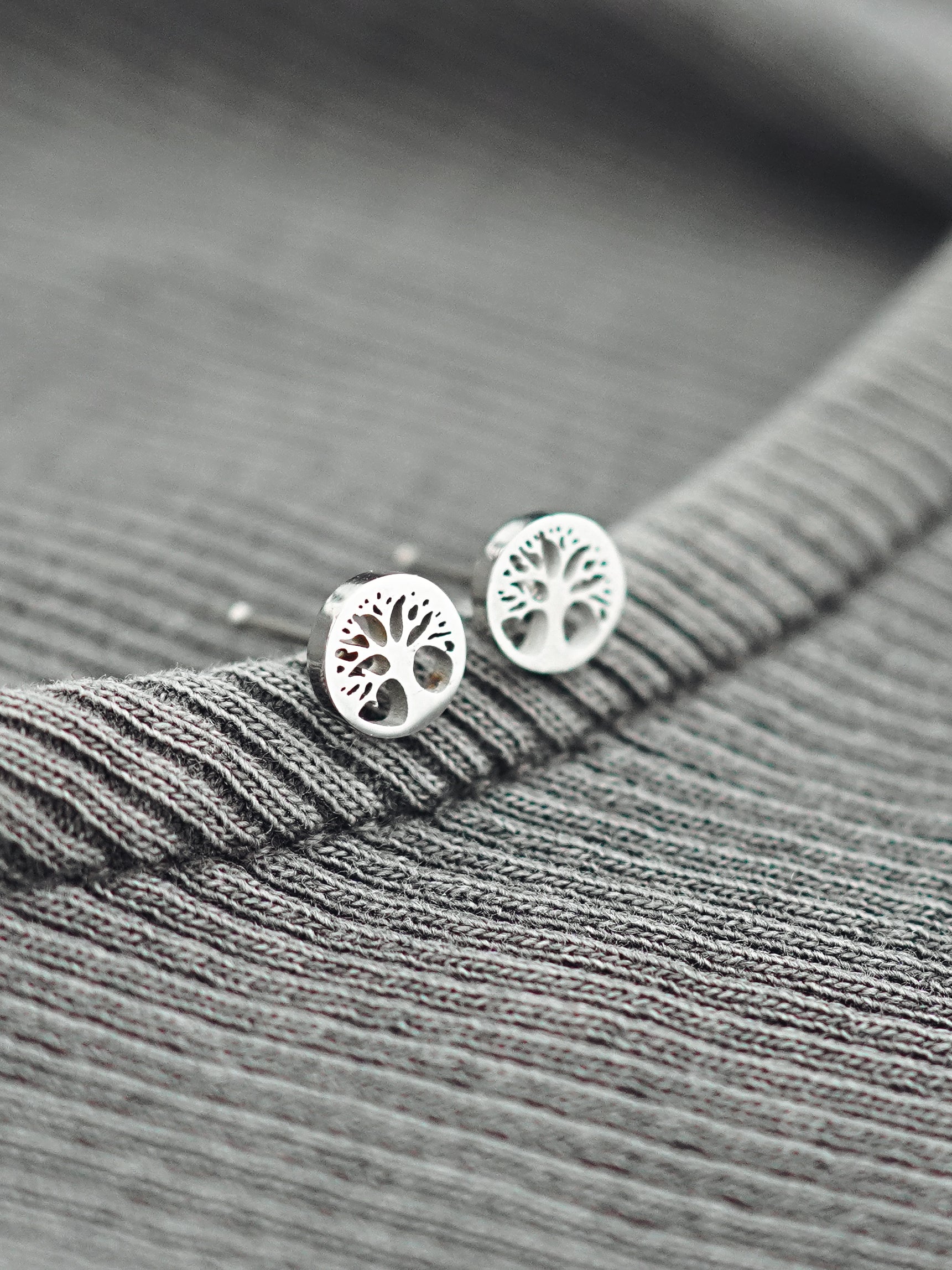 Silver tree-shaped earrings on a gray textured fabric background