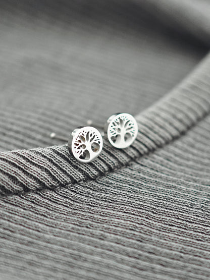 Silver tree-shaped earrings on a gray textured fabric background