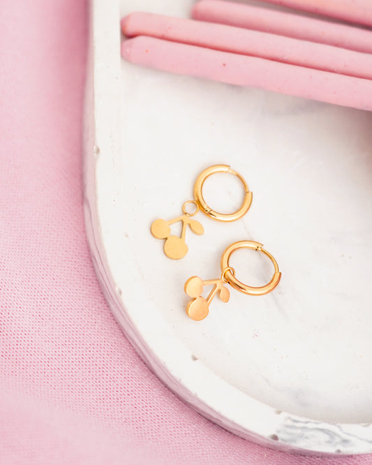 Gold hoop earrings on a white plate with pink background