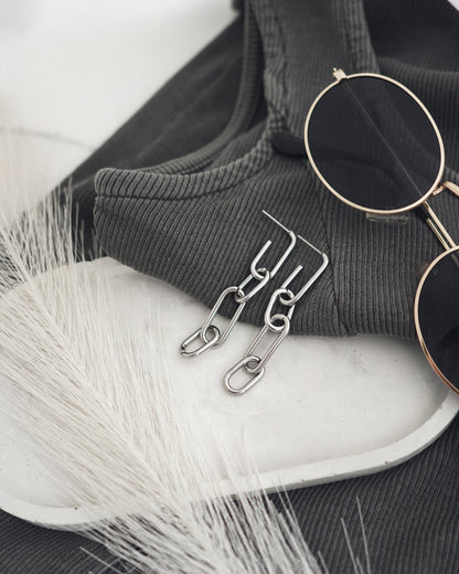Sunglasses and silver-plated earrings on a white surface with a black fabric background