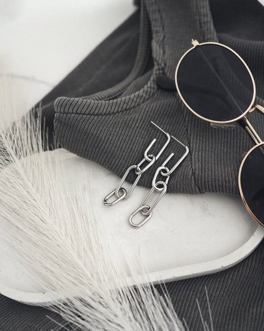 Sunglasses and silver-plated earrings on a white surface with a black fabric background