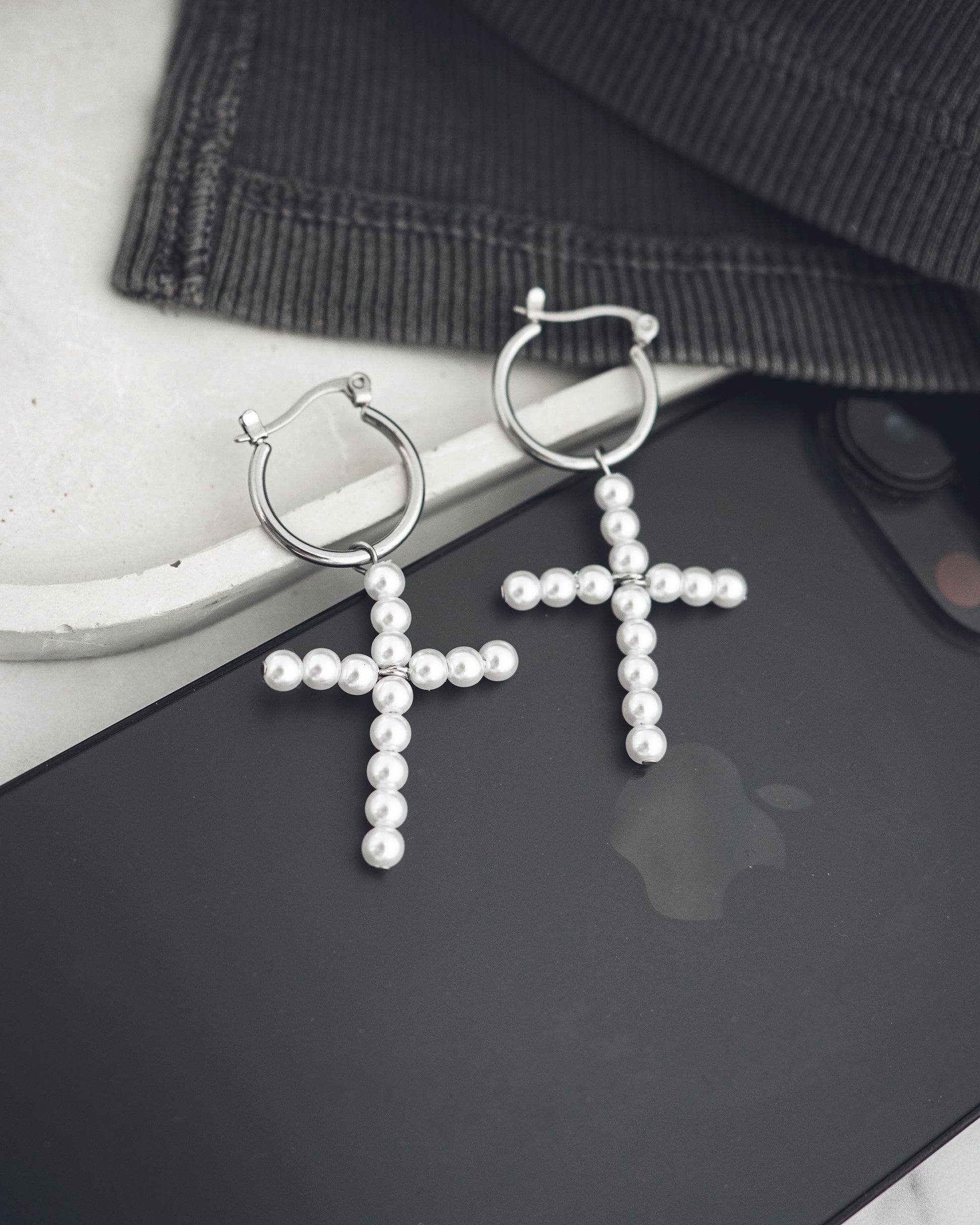 Pearl cross earrings on a black surface with a blurred background
