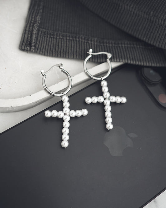 Pearl cross earrings on a black surface with a blurred background