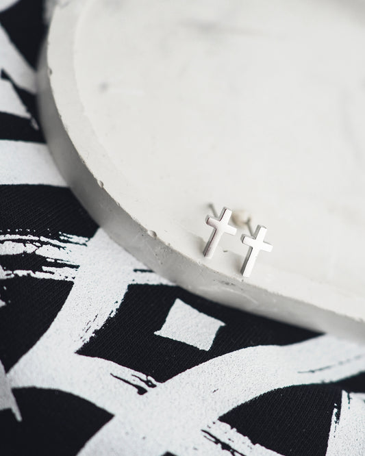 Silver cross earrings on a white surface with a black and white patterned fabric background