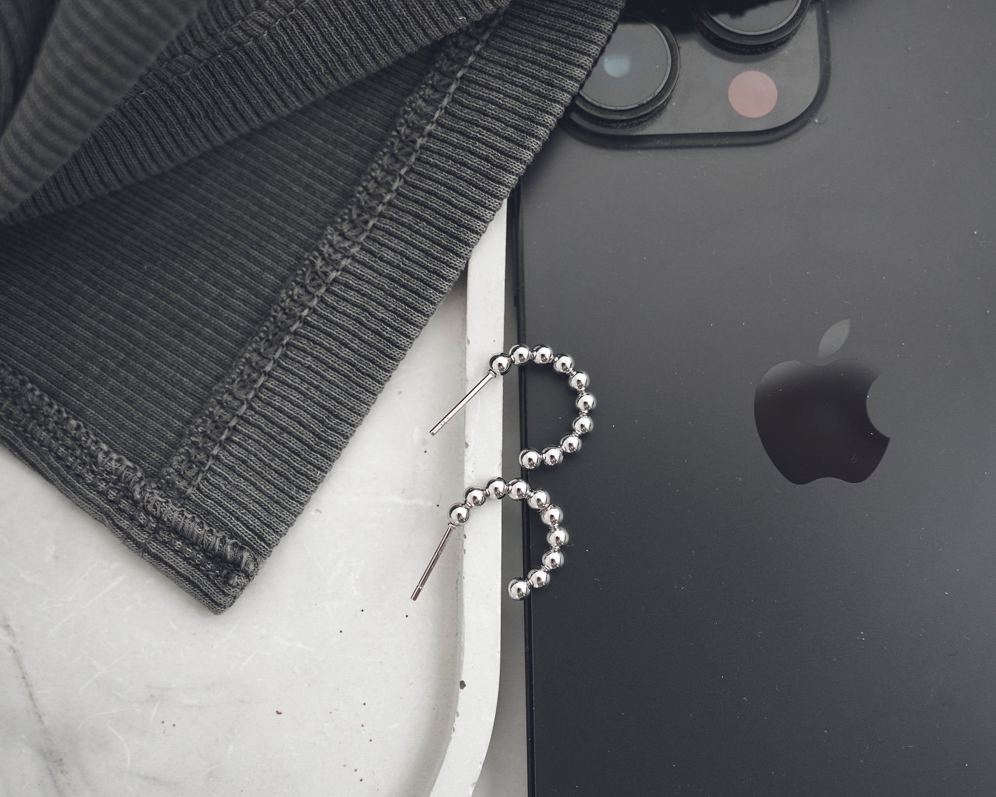Black smartphone with Apple logo next to a black beaded earring on a white surface