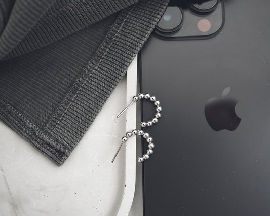 Black smartphone with Apple logo next to a black beaded earring on a white surface