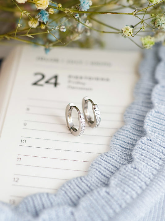 Silver hoop earrings on a calendar with flowers and a blue fabric background