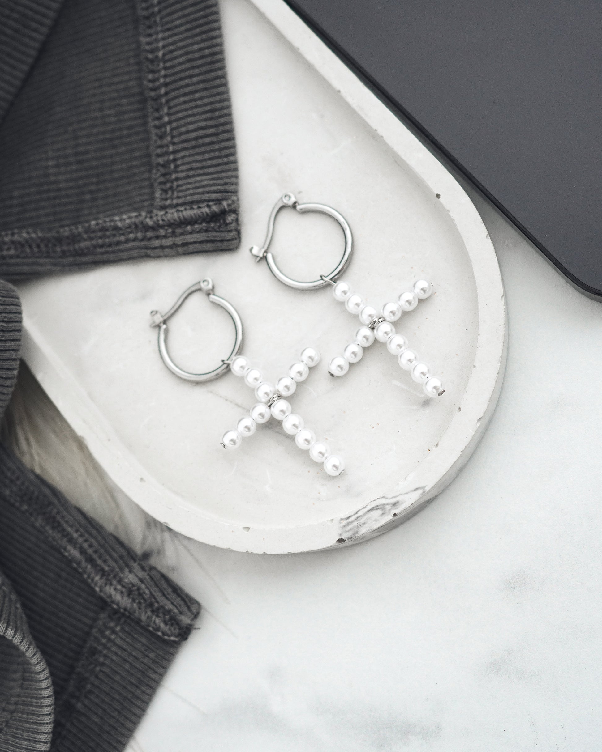 Silver hoop earrings with pearl crosses on a white surface