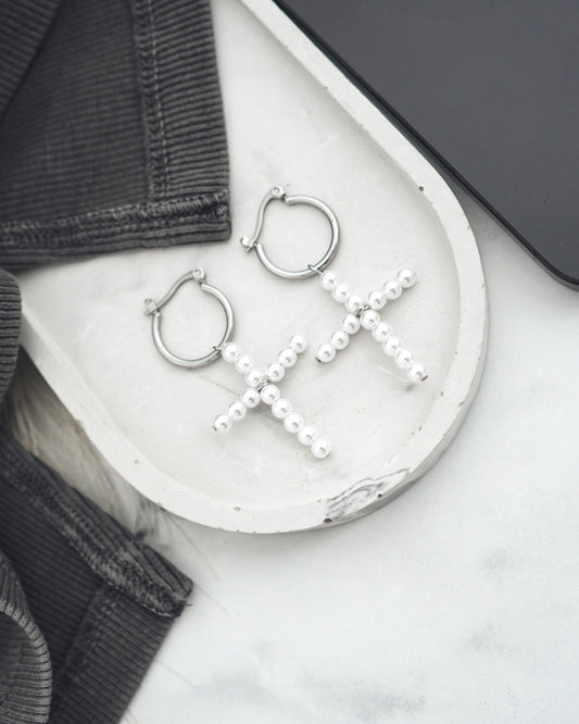 Silver hoop earrings with pearl crosses on a white surface