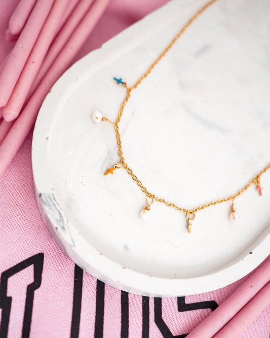 Gold necklace with colorful charms on a white stone surface with pink background