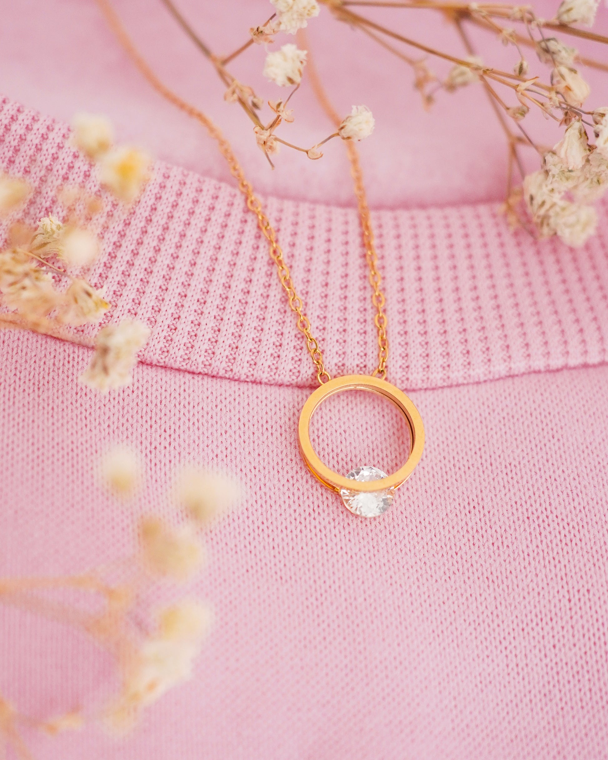 Gold necklace with a circular pendant on a pink fabric background