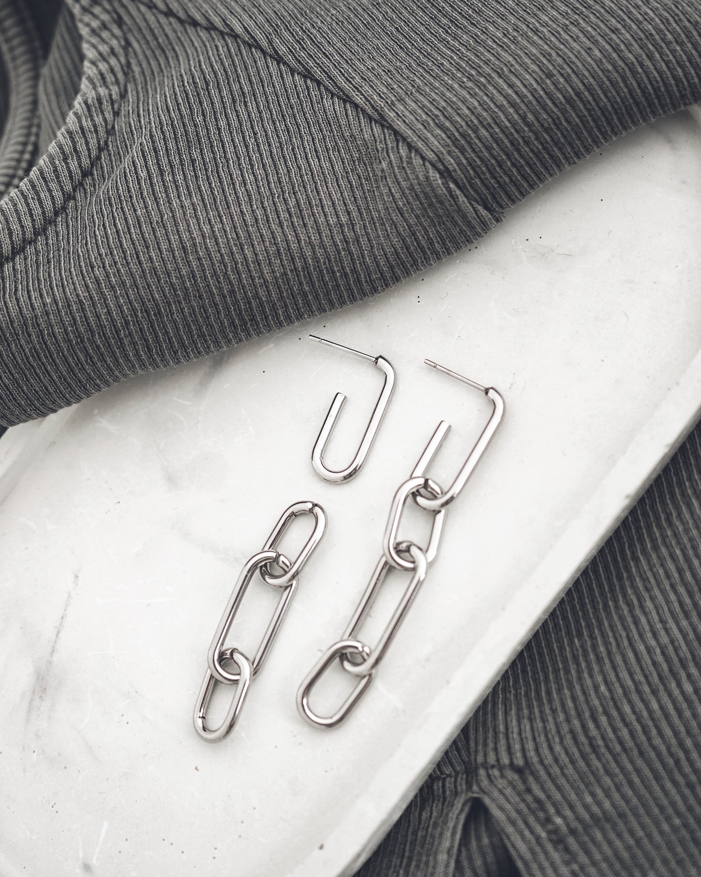 Silver chain earrings on a textured surface with gray fabric in the background