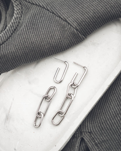 Silver chain earrings on a textured surface with gray fabric in the background