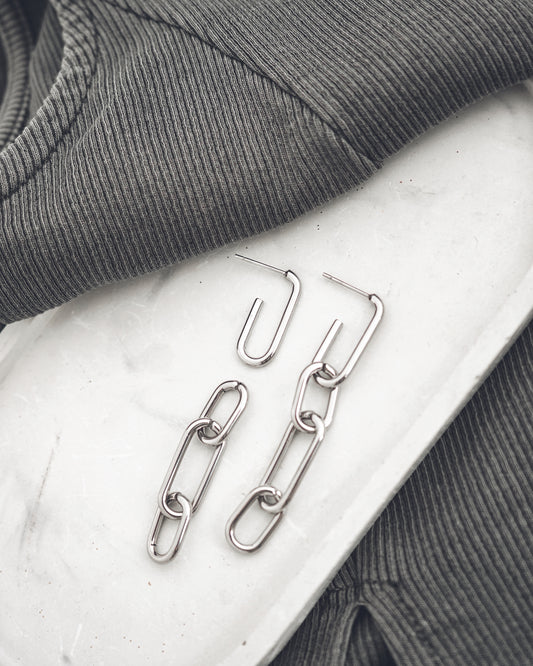 Silver chain earrings on a textured surface with gray fabric in the background