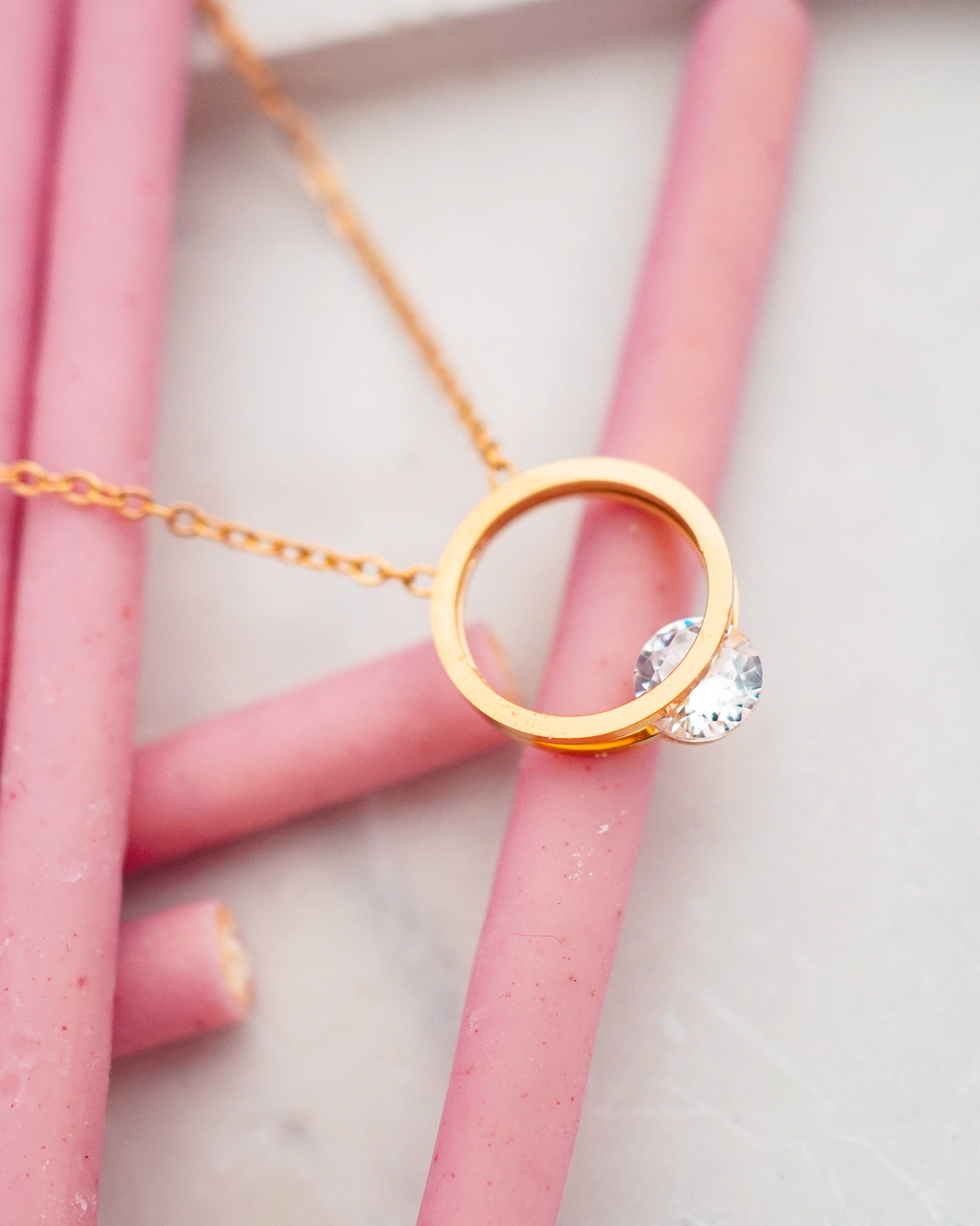 Gold colored necklace with a circular pendant on pink straws