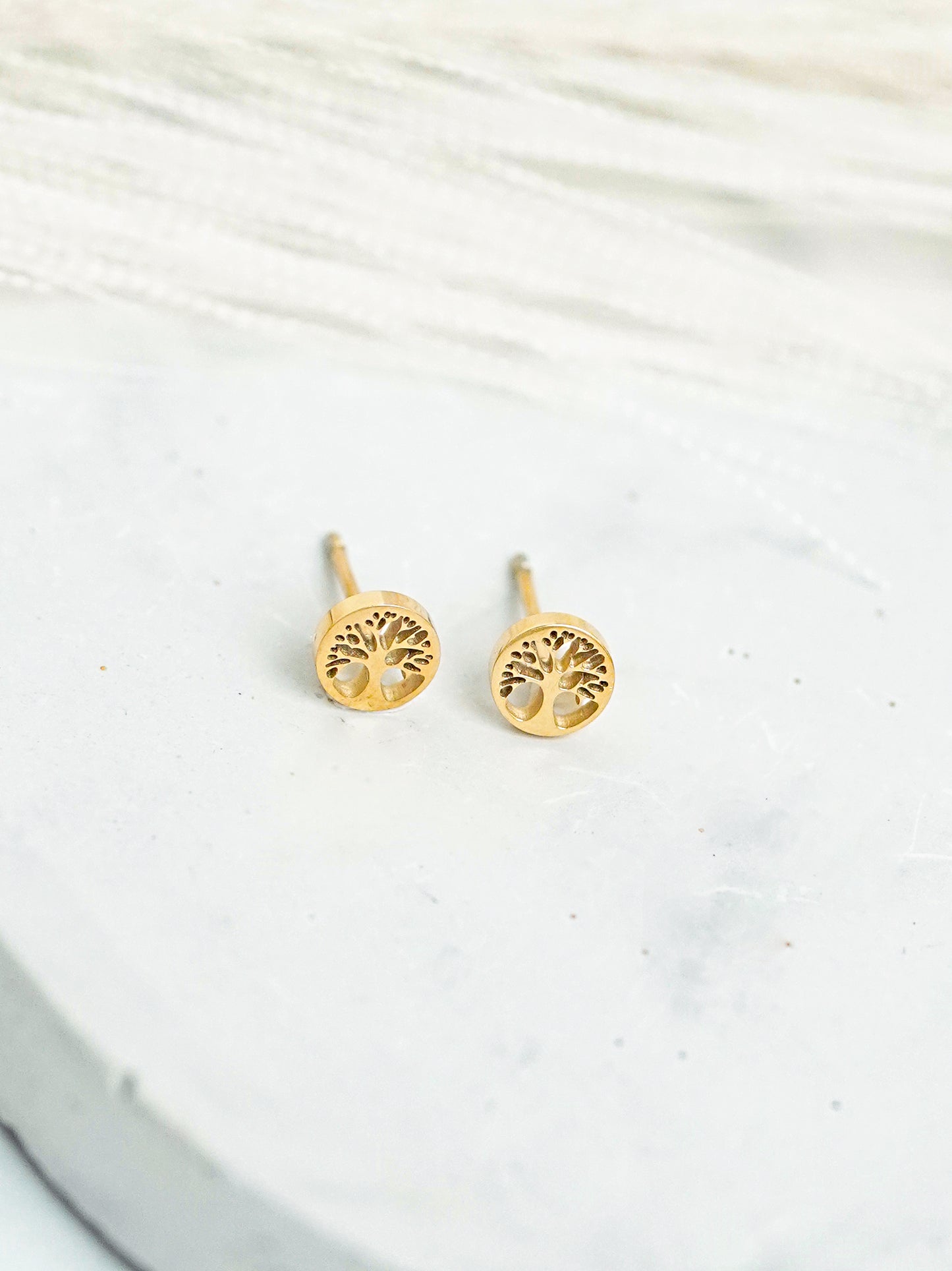 Gold-plated tree-shaped earrings on a white fabric background