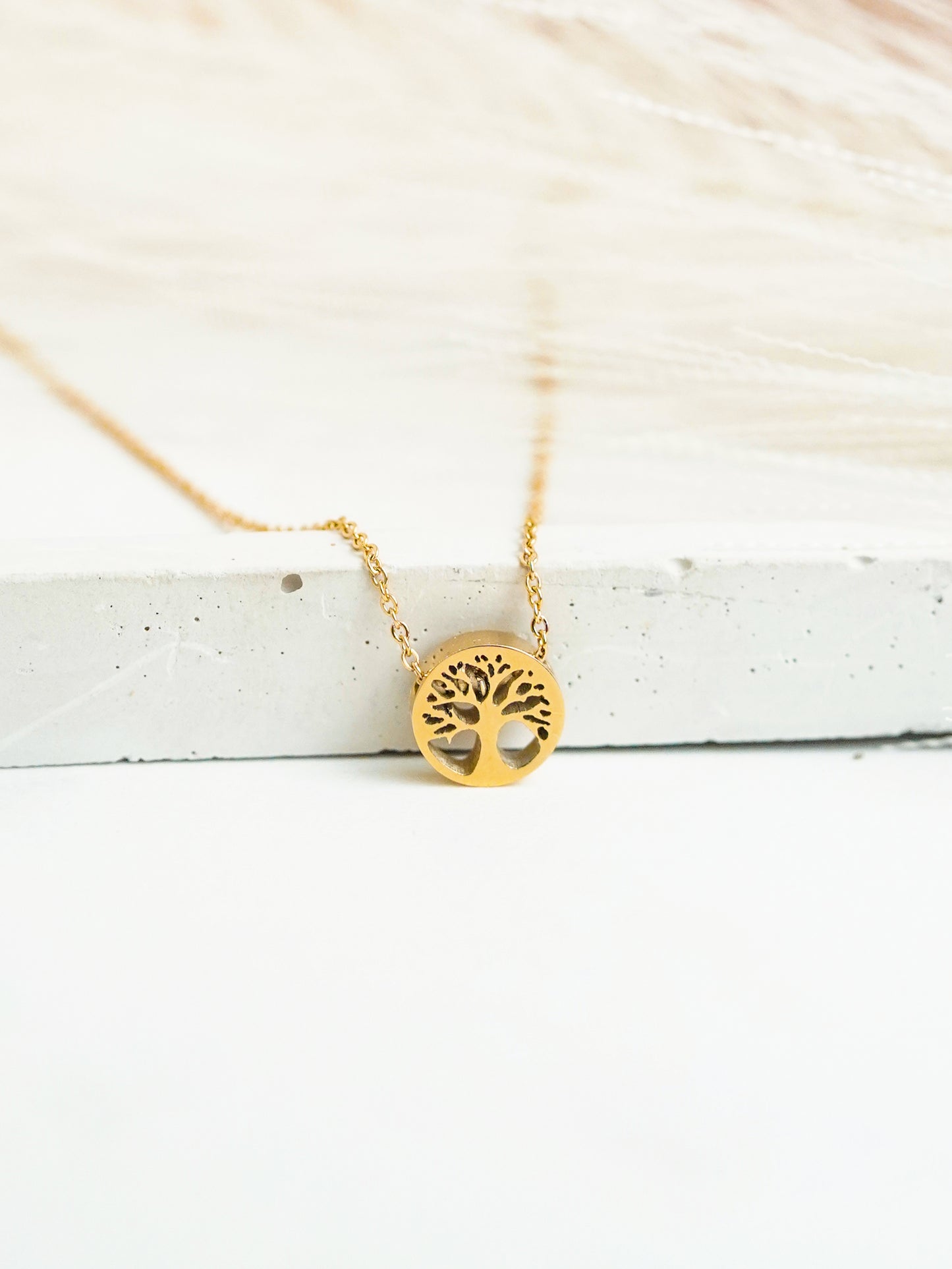 Gold tree of life necklace on a white wooden surface