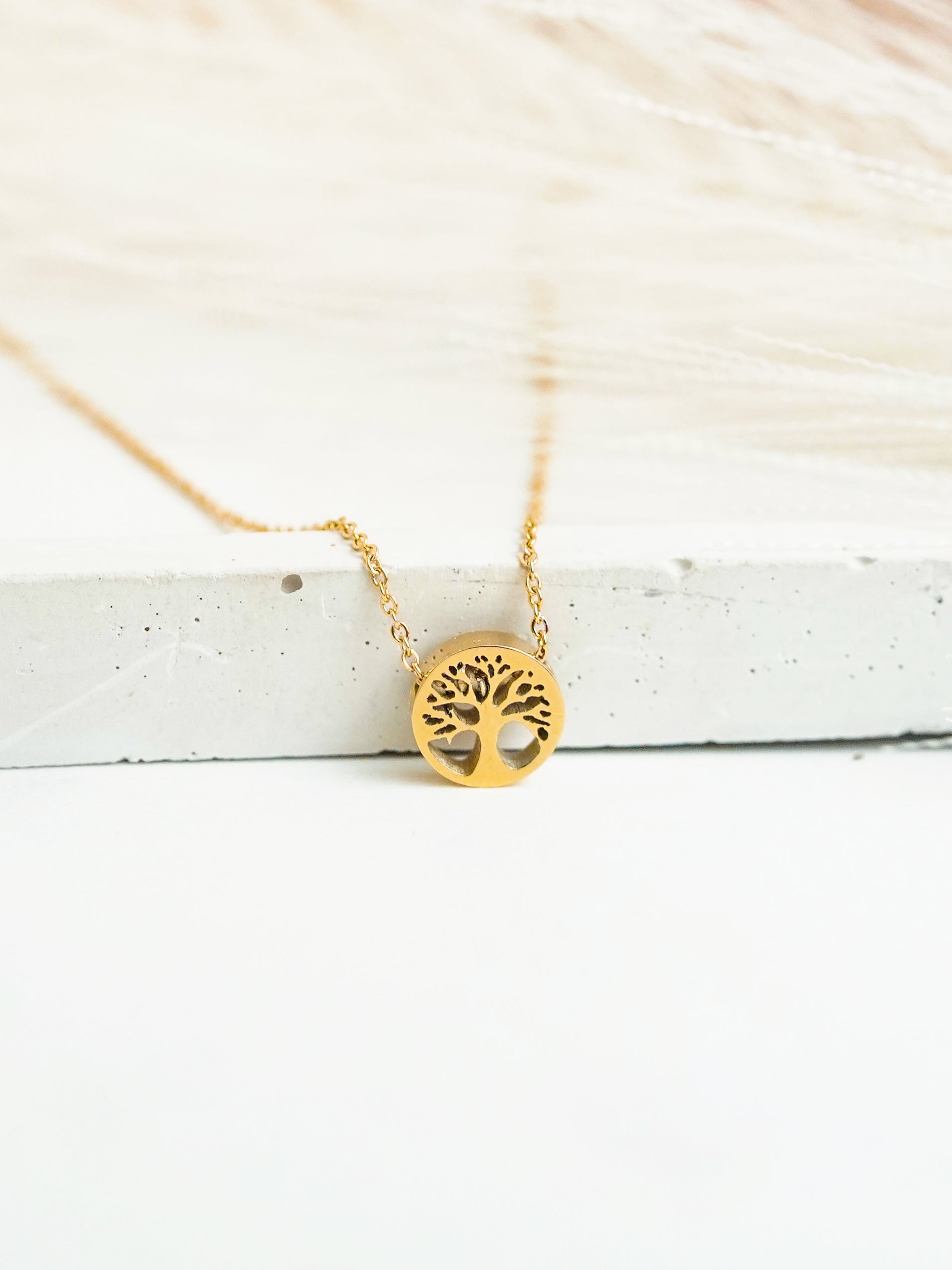 Gold tree of life necklace on a white wooden surface