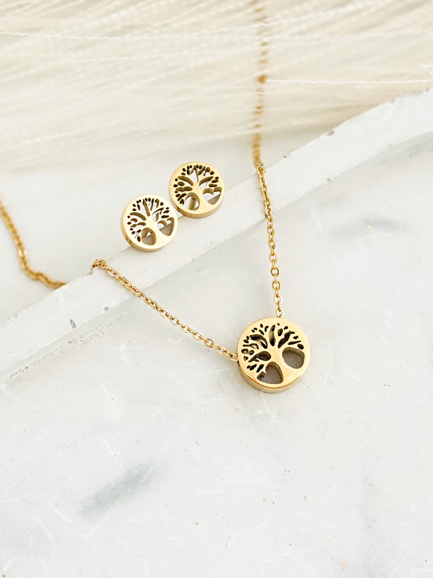 Gold-colored necklace and earrings with tree-of-life design on a white surface