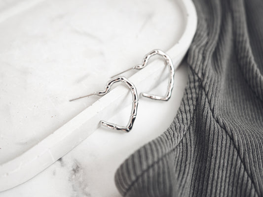 Silver heart-shaped earrings on a white marble surface with a gray fabric background