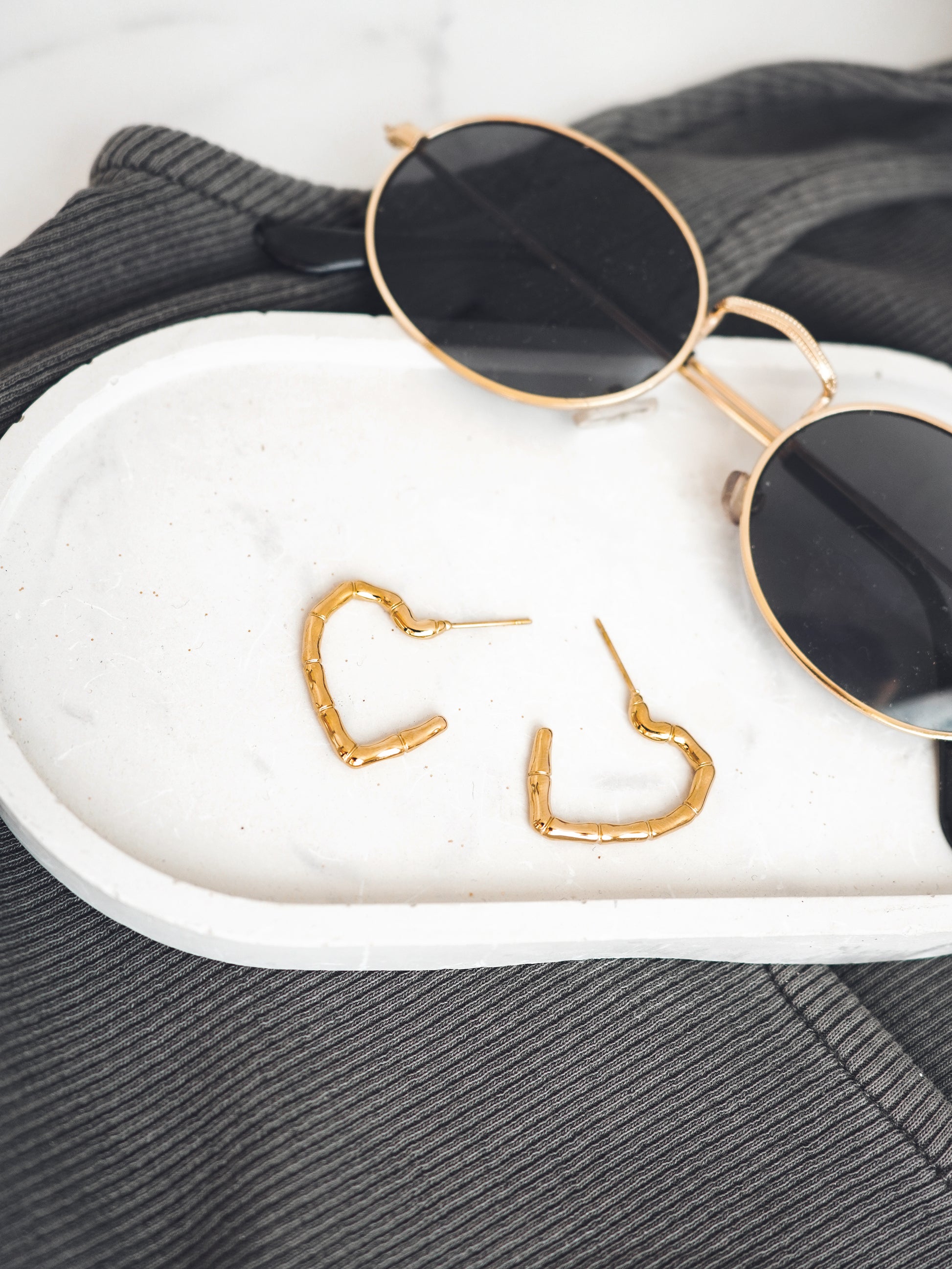 Gold colored heart-shaped earrings on a white surface with sunglasses in the background