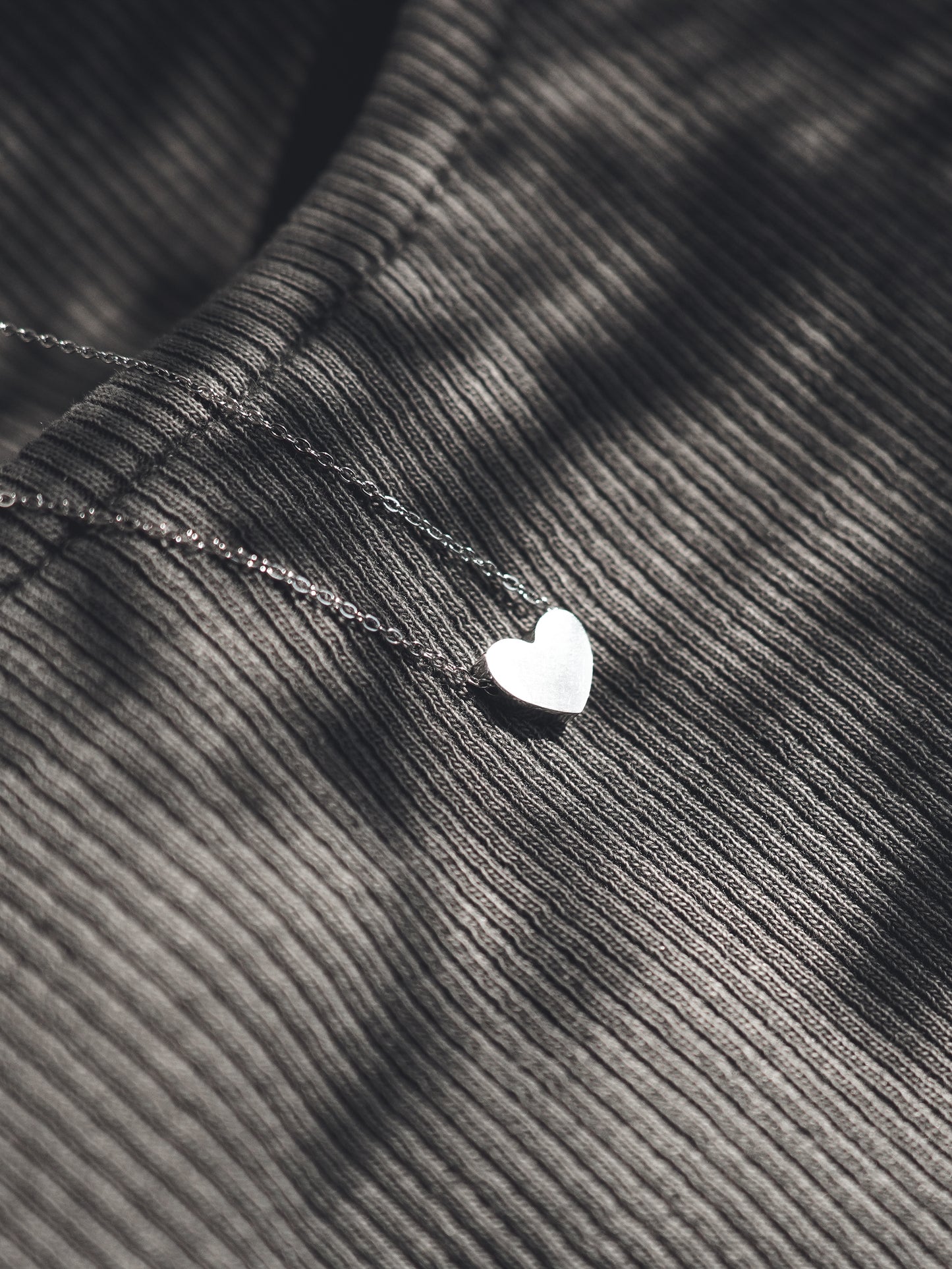 Silver heart-shaped pendant on a chain against a textured fabric background