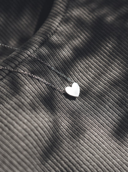 Silver heart-shaped pendant on a chain against a textured fabric background