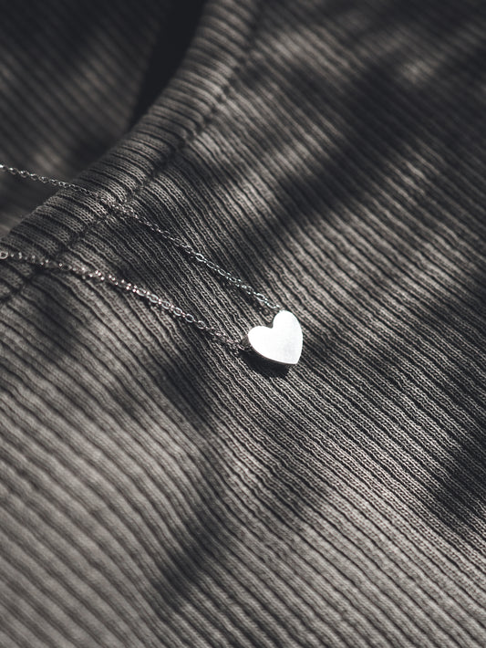 Silver heart-shaped pendant on a chain against a textured fabric background
