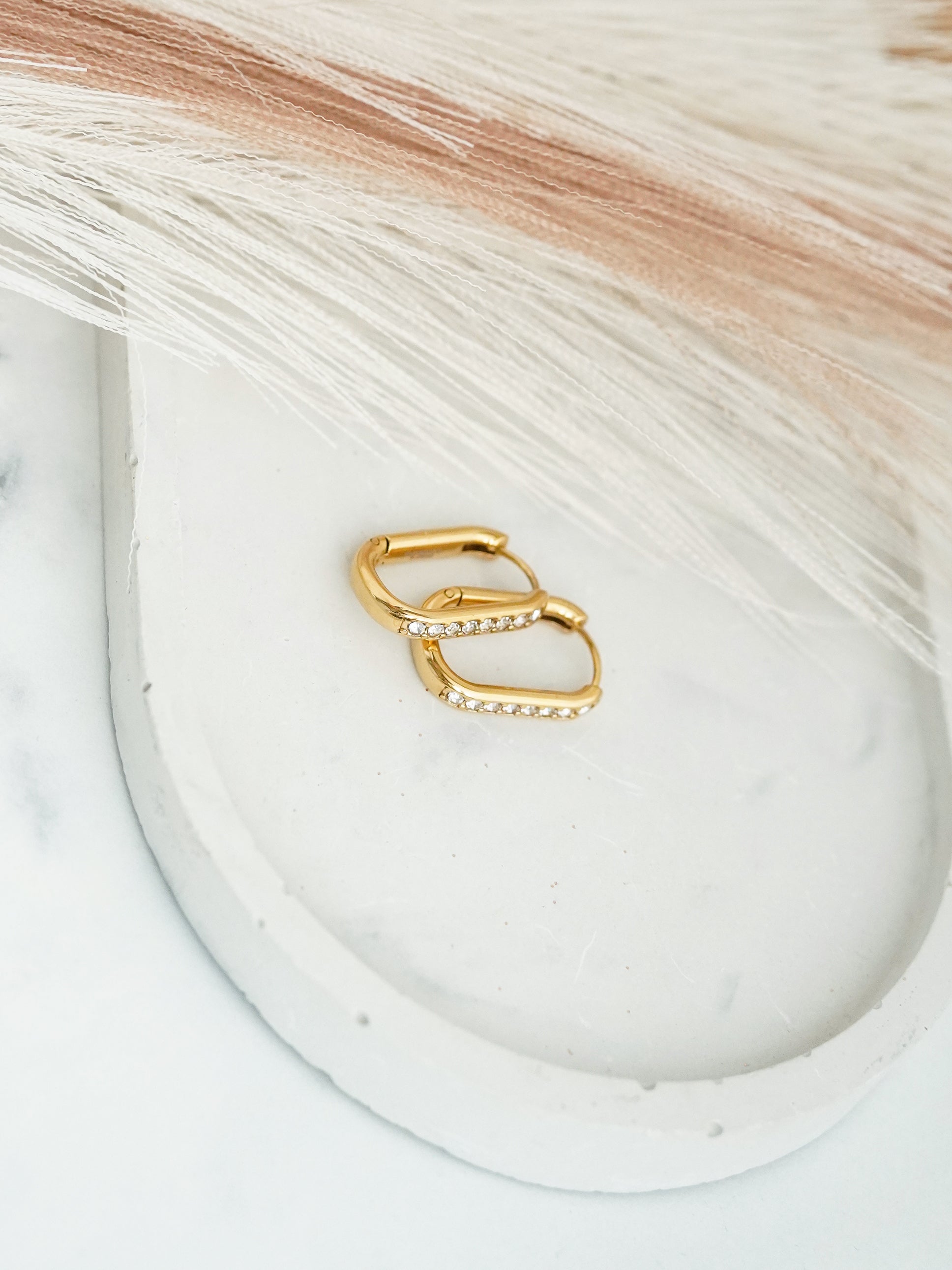 Gold- plated hoop earrings on a white dish with a textured background