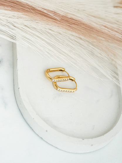 Gold- plated hoop earrings on a white dish with a textured background
