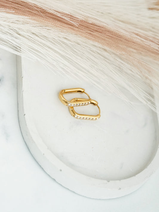 Gold- plated hoop earrings on a white dish with a textured background